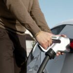 Imagem mostra mãos masculinas em carregador de carro elétrico