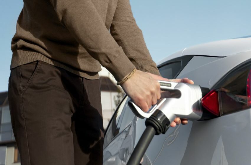 Imagem mostra mãos masculinas em carregador de carro elétrico