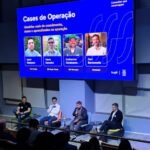 Imagem mostra quatro executivos em palco com telão ao fundo