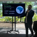Rica Legname, cofundador da Spott, em pé em frente a uma TV apresentando dados sobre infraestrutura de eletropostos