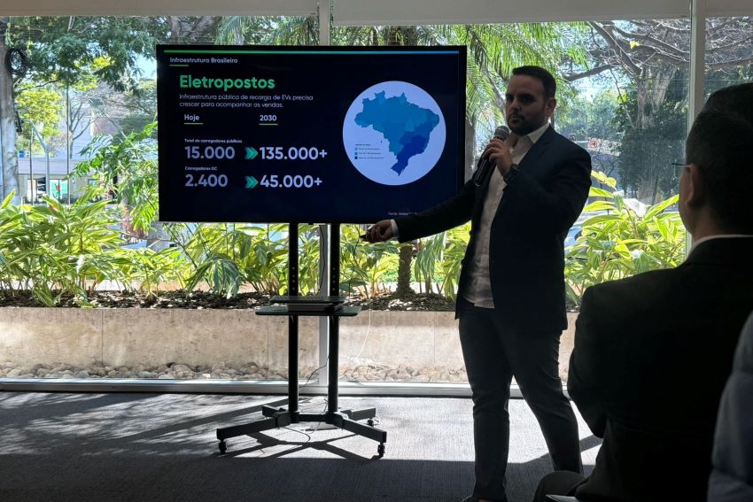 Rica Legname, cofundador da Spott, em pé em frente a uma TV apresentando dados sobre infraestrutura de eletropostos