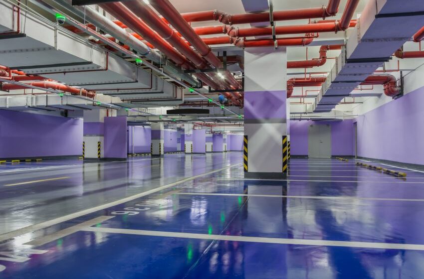 Imagem mostra estacionamento coberto com vagas coloridas e tubulação para chuveiros automáticos no alto
