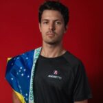 Piloto Felipe Drugovich posa com camisa da Andretti e bandeira do Brasil no ombro direito