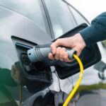 Imagem mostra mão de homem conectando plugue de carregador em carro elétrico