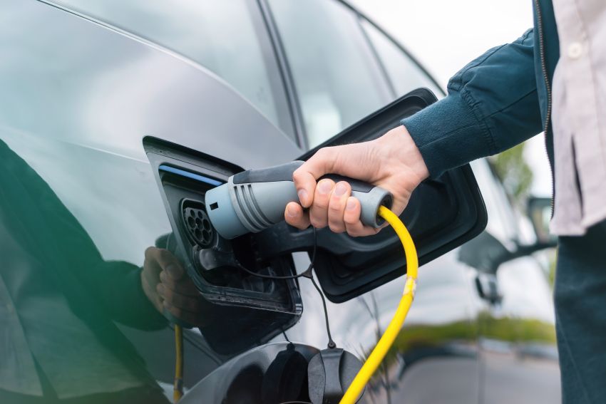 Imagem mostra mão de homem conectando plugue de carregador em carro elétrico