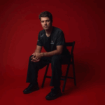 Felipe Drugovich está sentado em uma cadeira, em frente a um fundo vermelho