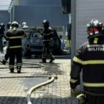 imagem mostra carro destruído pelas chamas e bombeiros em volta