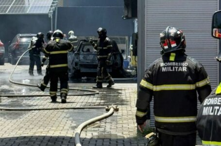 imagem mostra carro destruído pelas chamas e bombeiros em volta