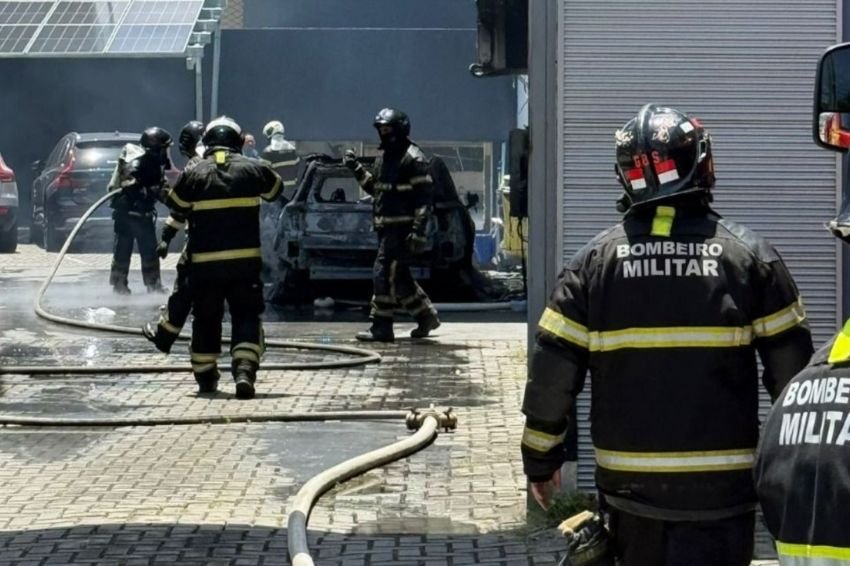 imagem mostra carro destruído pelas chamas e bombeiros em volta