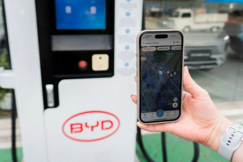Mão masculina segura smartphine com o app BYD Recharge em frente a carregador